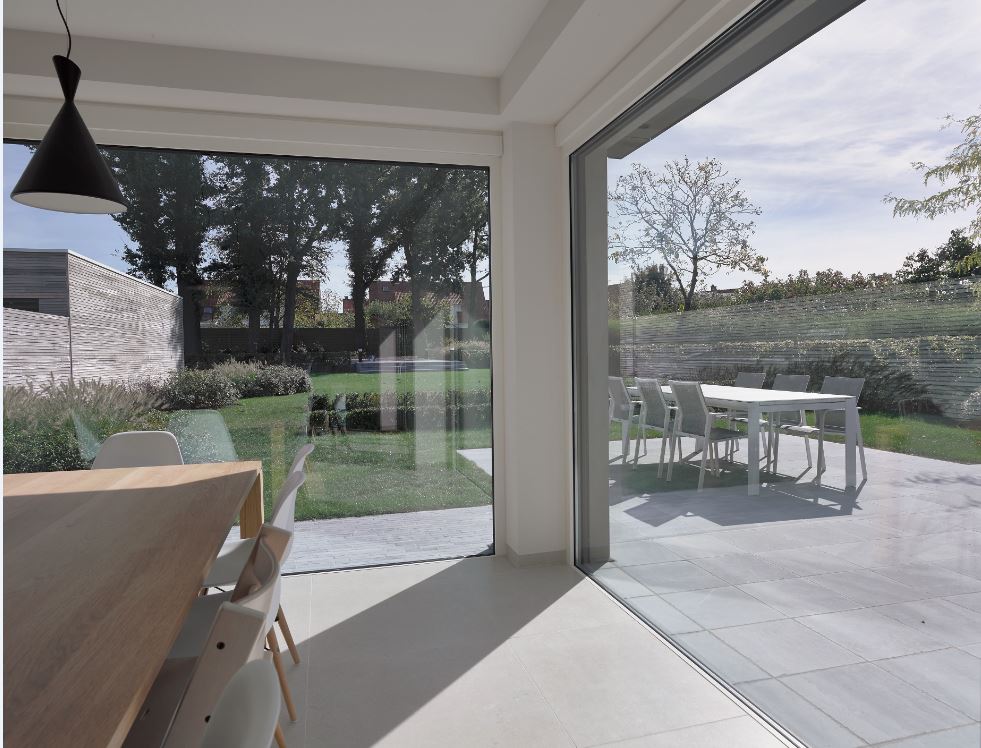salle à manger ouverte avec de grandes fenêtres en aluminium blanc donnant sur la terrasse et le jardin