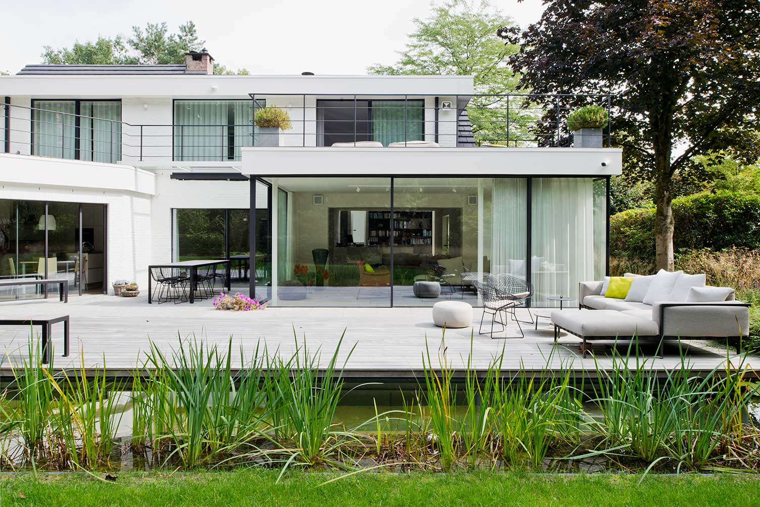 witte villa met grote zwarte aluminium ramen met grote glaspartijen met zicht op terras en vijver
