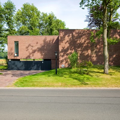 Une maison en brique placée sur une pelouse verte avec quelques arbres. 