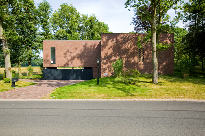 Une maison en brique placée sur une pelouse verte avec quelques arbres. 