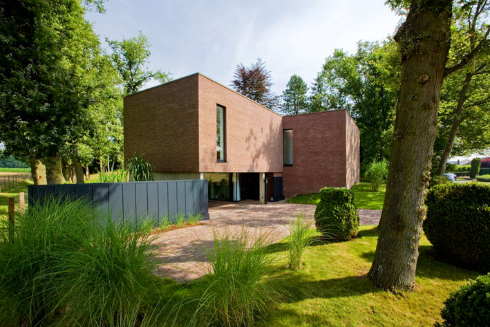 Une maison carrée en briques sur une pelouse avec quelques arbres.
