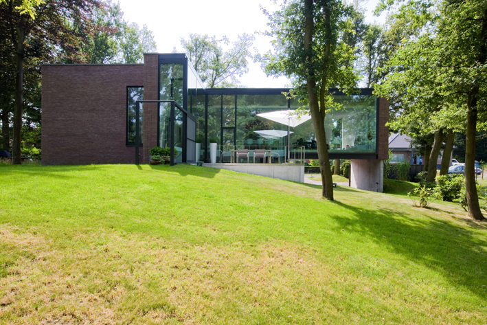 a brick, glass and aluminium house sits on a grassy hill. There is trees surrounding the property.
